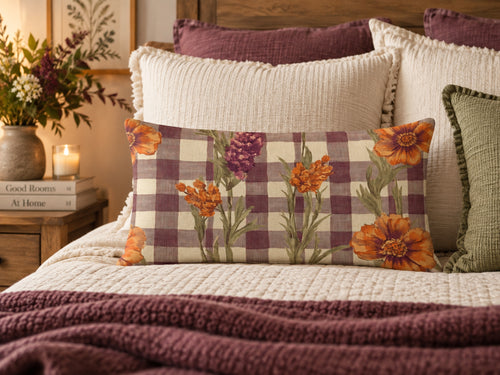 A rectangular decorative throw pillow with a purple and beige gingham pattern and orange floral print, styled on a bed with other pillows and a blanket.