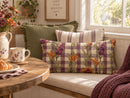 A cozy indoor nook with a floral and gingham throw pillow on a cushioned bench, alongside other decorative pillows, a wooden table with a floral mug, and a window in the background.