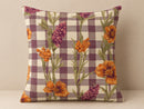 A square throw pillow featuring a purple and cream gingham check pattern overlaid with a botanical print of orange flowers and purple conifers, set against a neutral beige background.