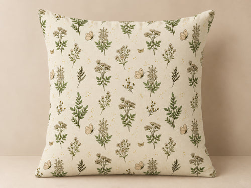 A square throw pillow with a cream-colored fabric featuring an all-over botanical pattern of green leaves, small wildflowers, and butterflies, set against a neutral beige background.