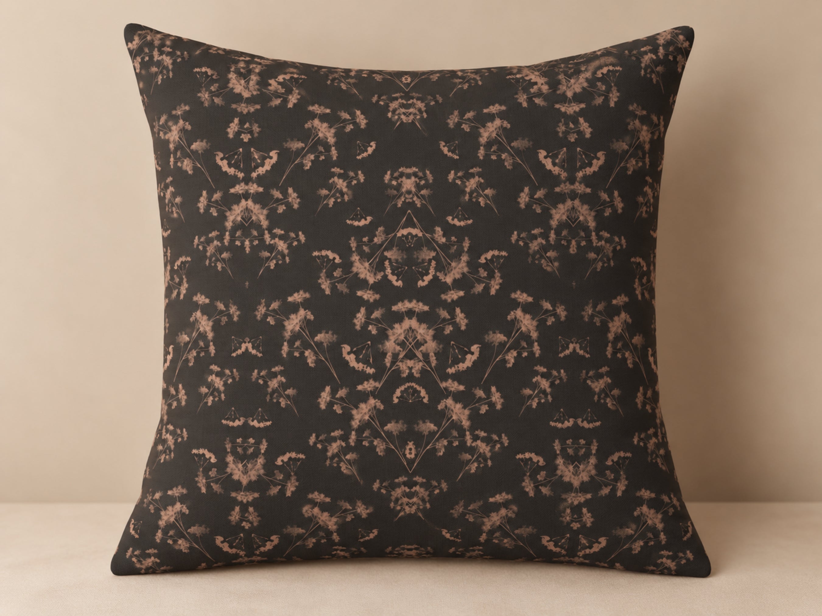 A square throw pillow with a dark charcoal background and a symmetrical beige damask floral pattern, set against a neutral beige background.