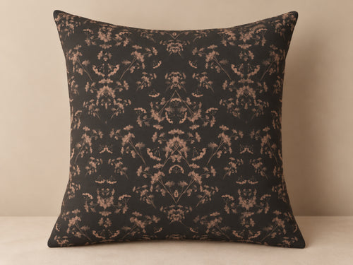 A square throw pillow with a dark charcoal background and a symmetrical beige damask floral pattern, set against a neutral beige background.