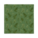 A square fabric item, likely a placemat or napkin, featuring a repeating pattern of green ferns and small white flowers on a muted sage green background.