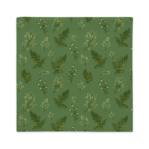 A square fabric item, likely a placemat or napkin, featuring a repeating pattern of green ferns and small white flowers on a muted sage green background.