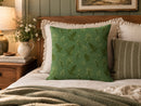A green decorative throw pillow with a delicate botanical leaf pattern, styled on a bed with white and striped pillows in a warm, cozy bedroom setting.