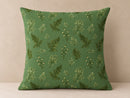 A square throw pillow with a green background and a repeating pattern of botanical ferns and small white flowers, set against a neutral beige background.