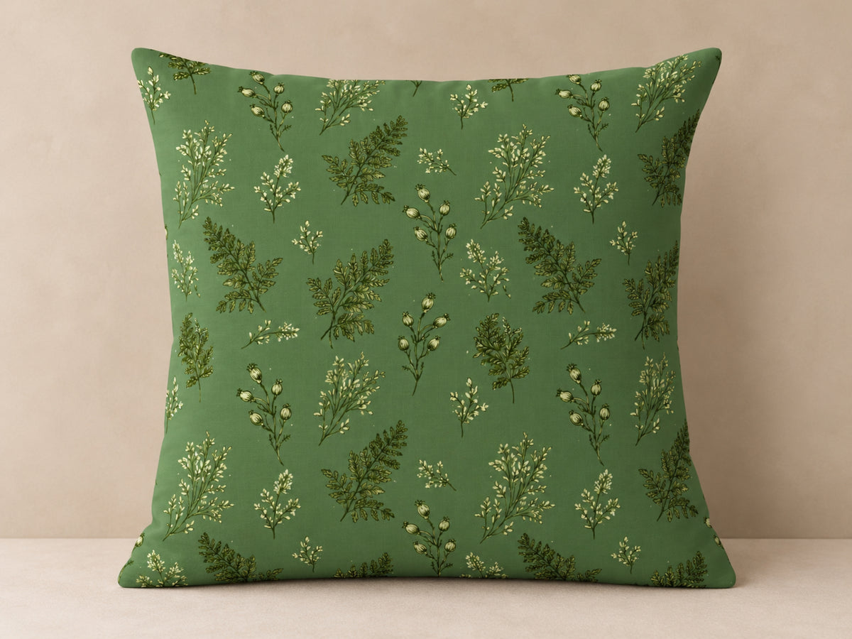 A square throw pillow with a green background and a repeating pattern of botanical ferns and small white flowers, set against a neutral beige background.