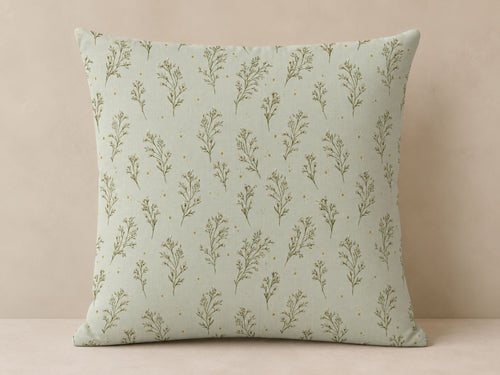 A square throw pillow with a sage green and olive green botanical pattern, set against a neutral beige background.
