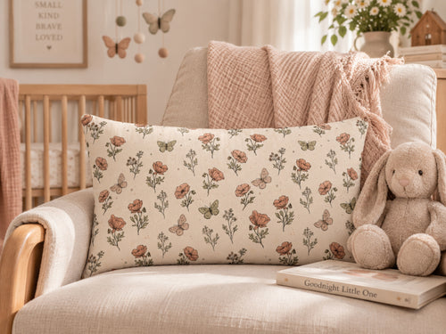 A rectangular throw pillow with a vintage-style floral and butterfly print in muted terracotta, olive green, and beige, styled on a cream-colored armchair next to a plush bunny toy and a soft pink blanket.